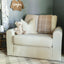 Light beige loveseat with a teddy bear striped pillow and plaid blanket in a nursery with a gray wall